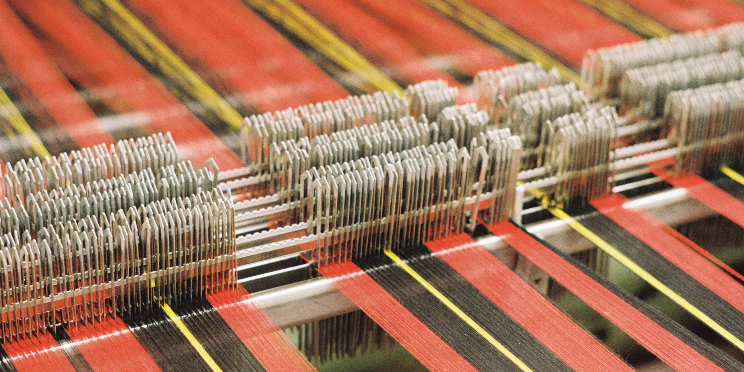 Black, red, and yellow wool strands being fed into a weaving machine.