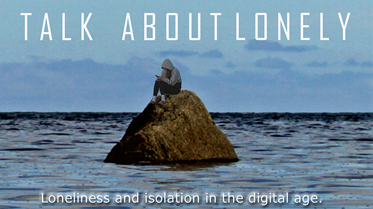 A hooded individual sits on a rock in the middle of the ocean.